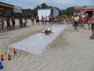 Una persona scivola su un telo in spiaggia, circondata da spettatori e coni colorati.