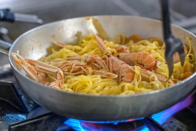 Pasta con crostacei in padella su fornello acceso.
