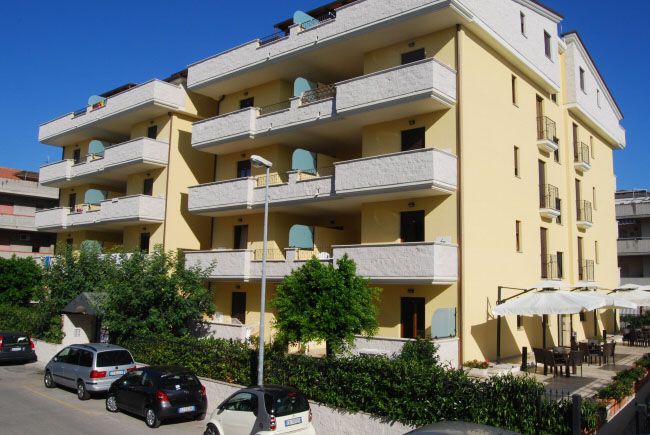 Edificio residenziale beige con balconi e auto parcheggiate davanti.