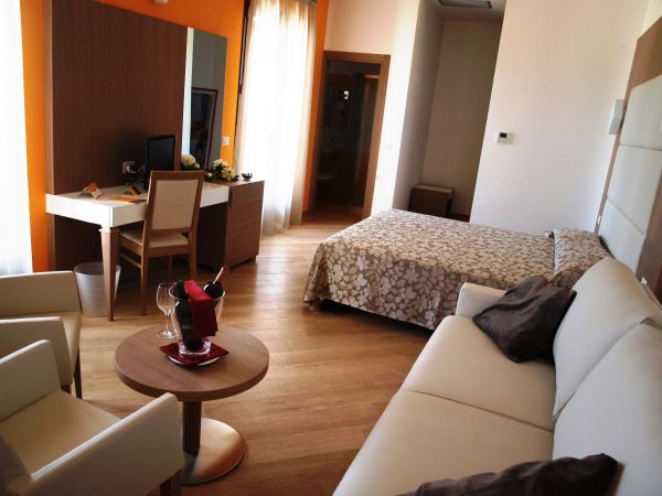 Camera con letto, divano, scrivania e accesso alla porta del balcone.