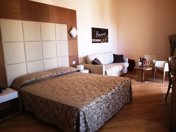 Camera con letto matrimoniale, testiera imbottita, divano bianco, tavolino e parete con quadro.