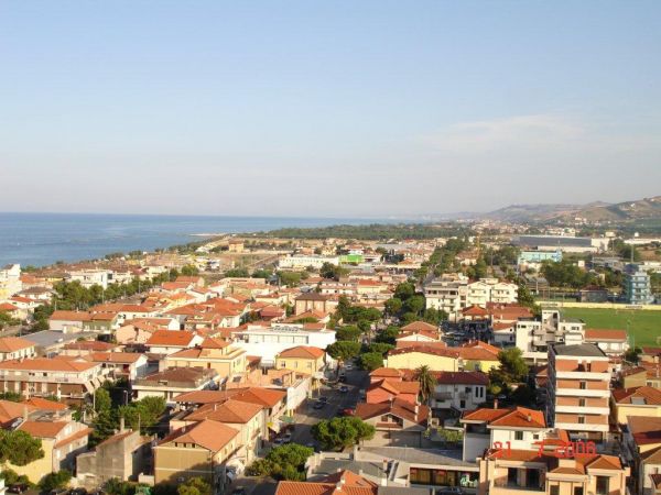 Vista panoramica di un'area costiera con case dai tetti rossi e il mare sullo sfondo.