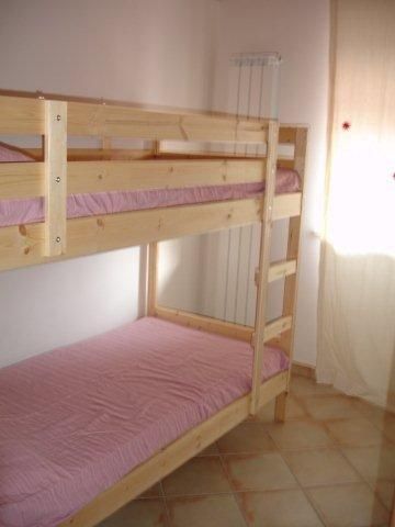Letto a castello in legno con coperte rosa in una stanza luminosa con pavimento piastrellato.