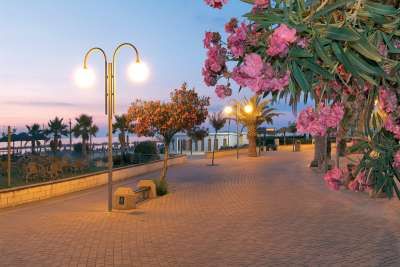Passeggiata al tramonto con lampioni accesi e oleandri fioriti.