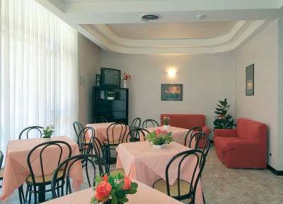 Sala da pranzo con tavoli decorati con fiori, pareti chiare e sedie nere.