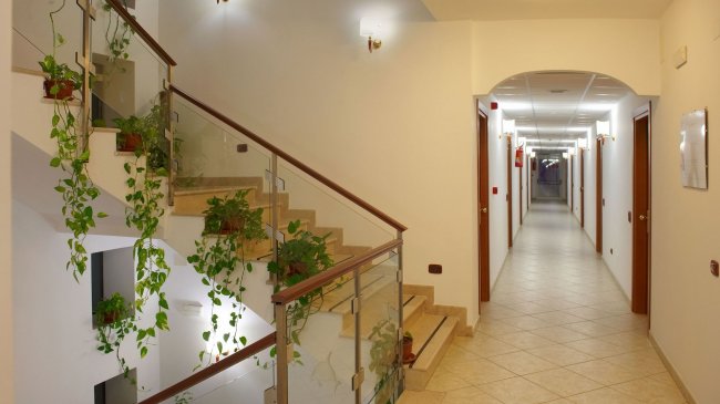 Corridoio con scala, pareti bianche e piante.