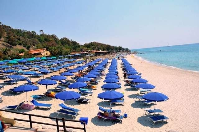 Spiaggia affollata con ombrelloni blu allineati lungo la costa.