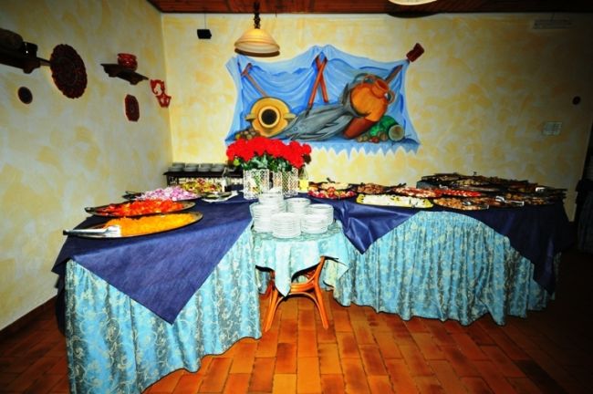 Tavoli riccamente decorati con teli blu e piatti di cibo, in una sala dal tema marinaro.