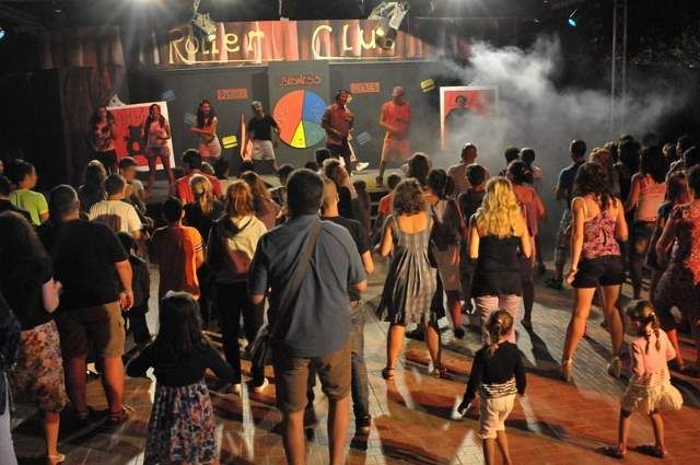 Persone ballano e si divertono di fronte a un palco con luci soffuse.