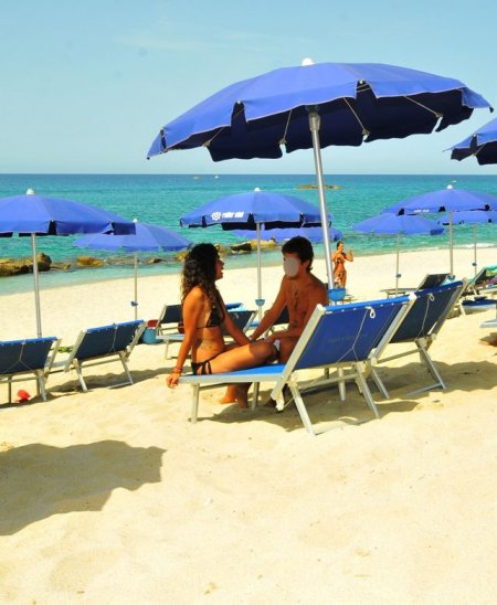 Due persone sotto ombrelloni blu in spiaggia.