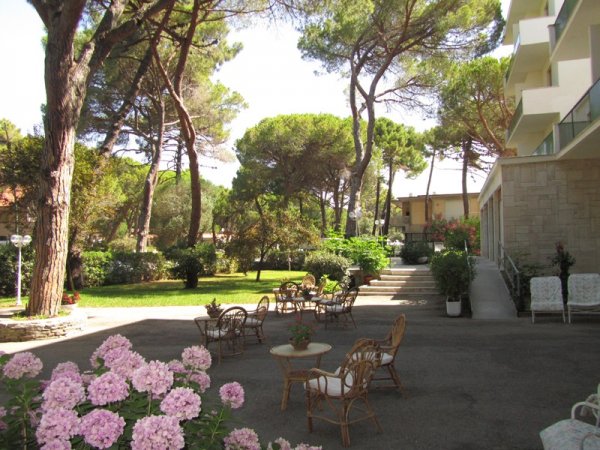 Giardino con tavoli e sedie in vimini, alberi e ortensie rosa.