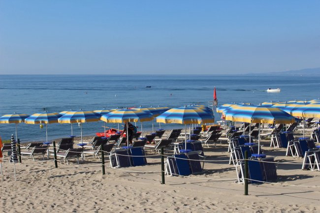 Spiaggia con file di lettini e ombrelloni giallo-blu.