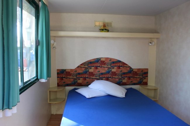 Letto blu con finestra e tende verdi a sinistra.