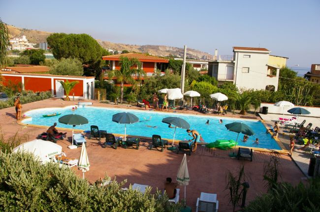 Una piscina circondata da lettini, ombrelloni e persone.