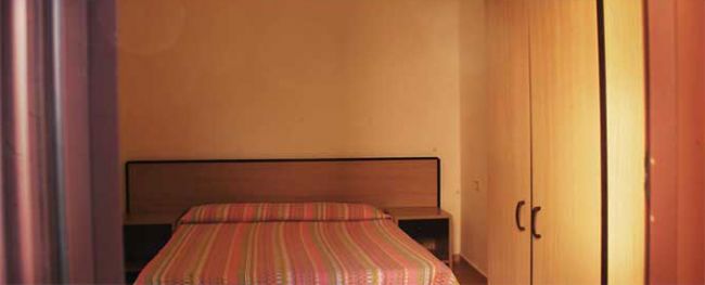 Camera da letto con letto matrimoniale a righe colorate e armadio in legno chiaro.