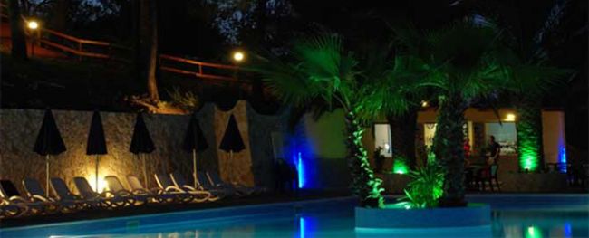 Piscina illuminata di notte, ombrelloni scuri.
