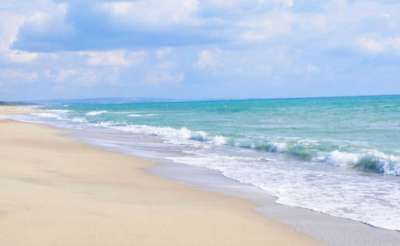 Una spiaggia sabbiosa con onde che si infrangono dolcemente e un cielo nuvoloso.