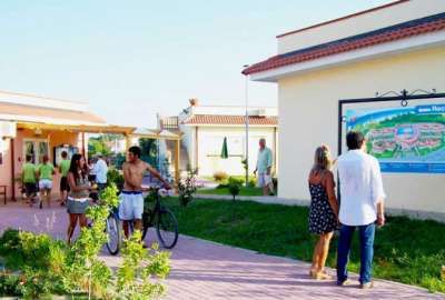 Persone passeggiano vicino a edifici e segnaletica in un complesso turistico.