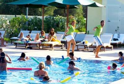 Persone nuotano in piscina mentre due adulti ballano a bordo vasca.