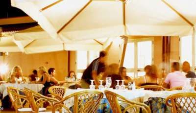 Persone sedute a tavoli con tovaglie bianche sotto grandi ombrelloni in un ristorante all'aperto.