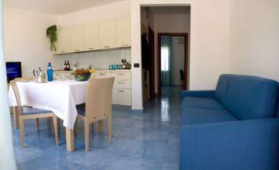 Soggiorno con divano blu, tavolo da pranzo e cucina a vista.