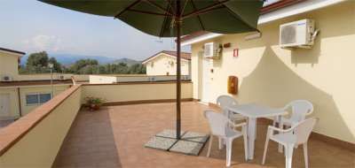 Terrazza con tavolo e sedie bianche sotto un ombrellone, vista su tetti.