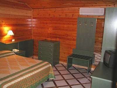 Camera in legno con letto matrimoniale, cassettiera e TV su pavimento a piastrelle.