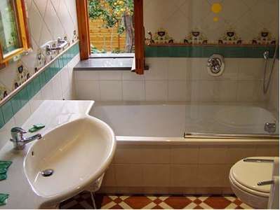 Bagno con vasca, lavandino, WC e finestra. Piastrelle bianche e dettagli decorativi.