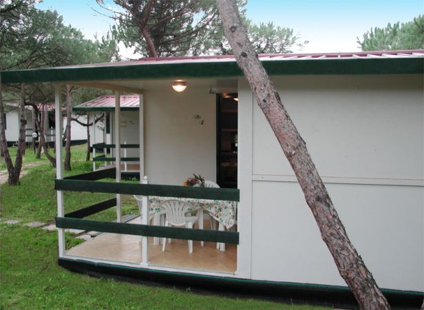 Veranda di una casa mobile con tavolo e sedie, circondata da alberi.