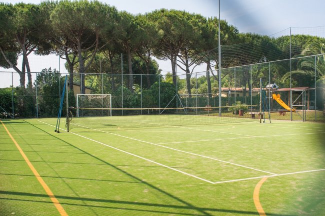 Campo da gioco verde con rete di recinzione e alberi sullo sfondo.