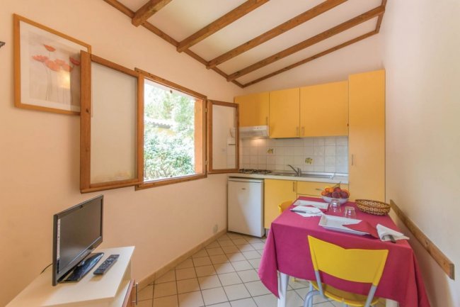 Cucina piccola con mobili gialli, finestra aperta, tavolo apparecchiato e TV.