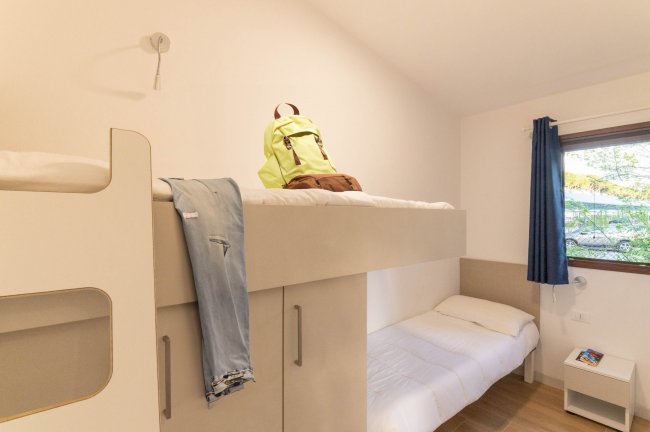 Stanza con letto a castello, zaino e jeans sul letto superiore.