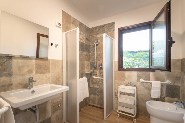 Bagno con lavabo, doccia, bidet e finestra; pareti in piastrelle decorate.