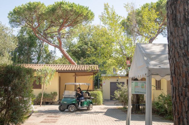 Persona su golf cart davanti a edifici gialli con giardino e pini alti.