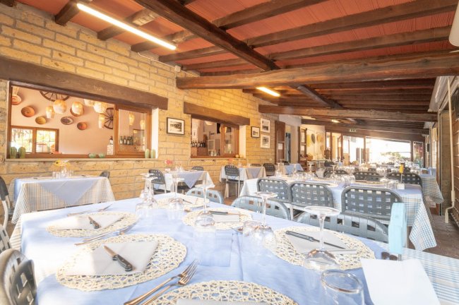 Interno di ristorante con tavoli apparecchiati, mattoni a vista e travi di legno.