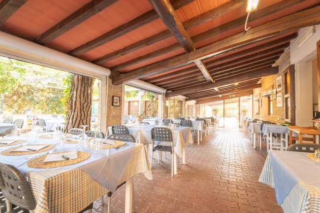 Sala ristorante con tavoli apparecchiati, travi a vista e ampie finestre.