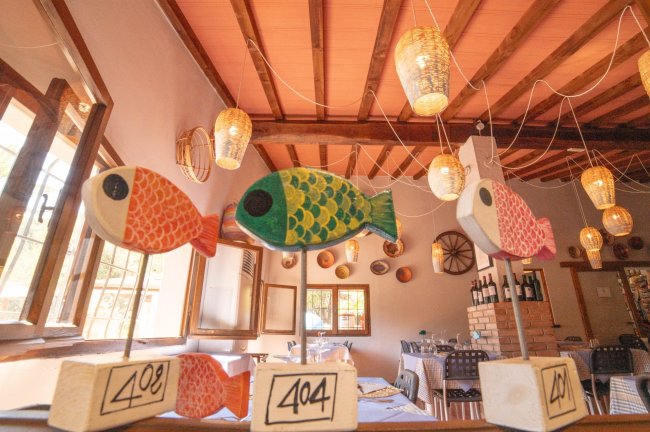 Tre pesci decorativi colorati su supporti, appesi in un ristorante con soffitto in legno e lanterne.