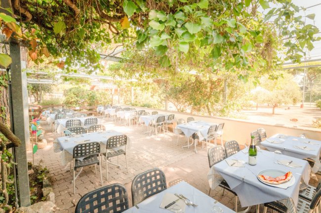 Giardino di un ristorante con tavoli apparecchiati sotto un pergolato ricoperto di foglie.