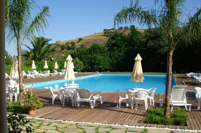 Piscina con ombrelloni e sedie su patio in legno.