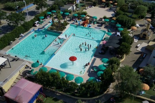 Veduta aerea di piscine con ombrelloni verdi.