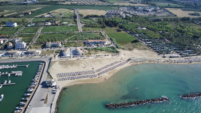 Spiaggia sabbiosa con ombrelloni e dintorni verdi.