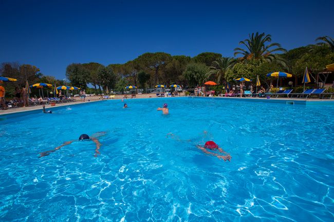 Persone che nuotano in una piscina all'aperto con ombrelloni gialli.