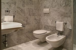 Un bagno con pareti e pavimento in marmo, lavabo, WC, bidet e portasciugamani bianco.