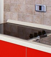 Un piano cottura nero con manopole su un mobiletto rosso davanti a una parete piastrellata beige.