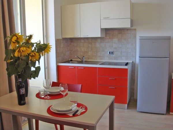 Piccola cucina moderna con mobili rossi, un tavolo apparecchiato e un mazzo di girasoli.