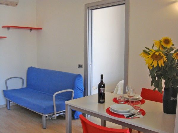 Soggiorno con divano blu, tavolo apparecchiato, fiori in vaso e sedia rossa.