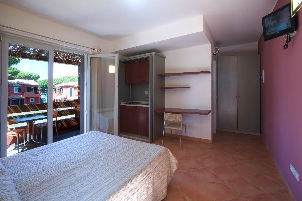 Camera con letto matrimoniale, scrivania, TV a muro e balcone. Vista su edifici rossi.