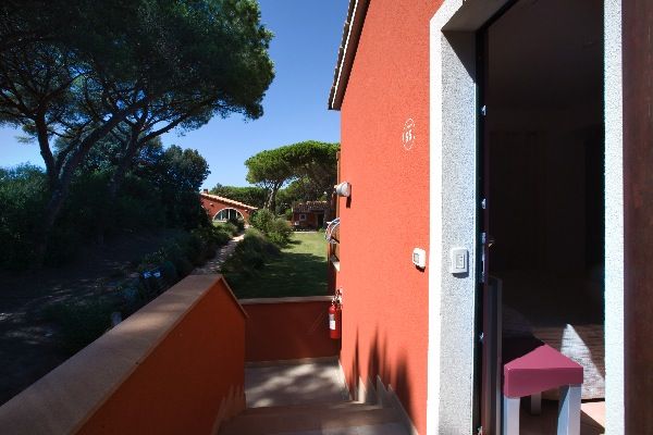 Entrata di un edificio arancio con giardino e pini sullo sfondo.