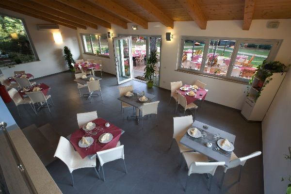 Sala da pranzo con tavoli apparecchiati, sedie bianche e finestre grandi.