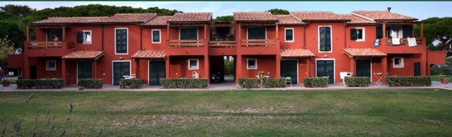 Un edificio a due piani color terracotta con terrazze e finestre, circondato da un prato verde.